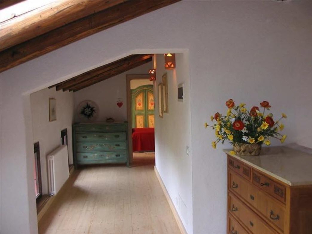 A narrow hallway with wooden beams on the ceiling, a wooden dresser with drawers, and a vase of flowers on a table.