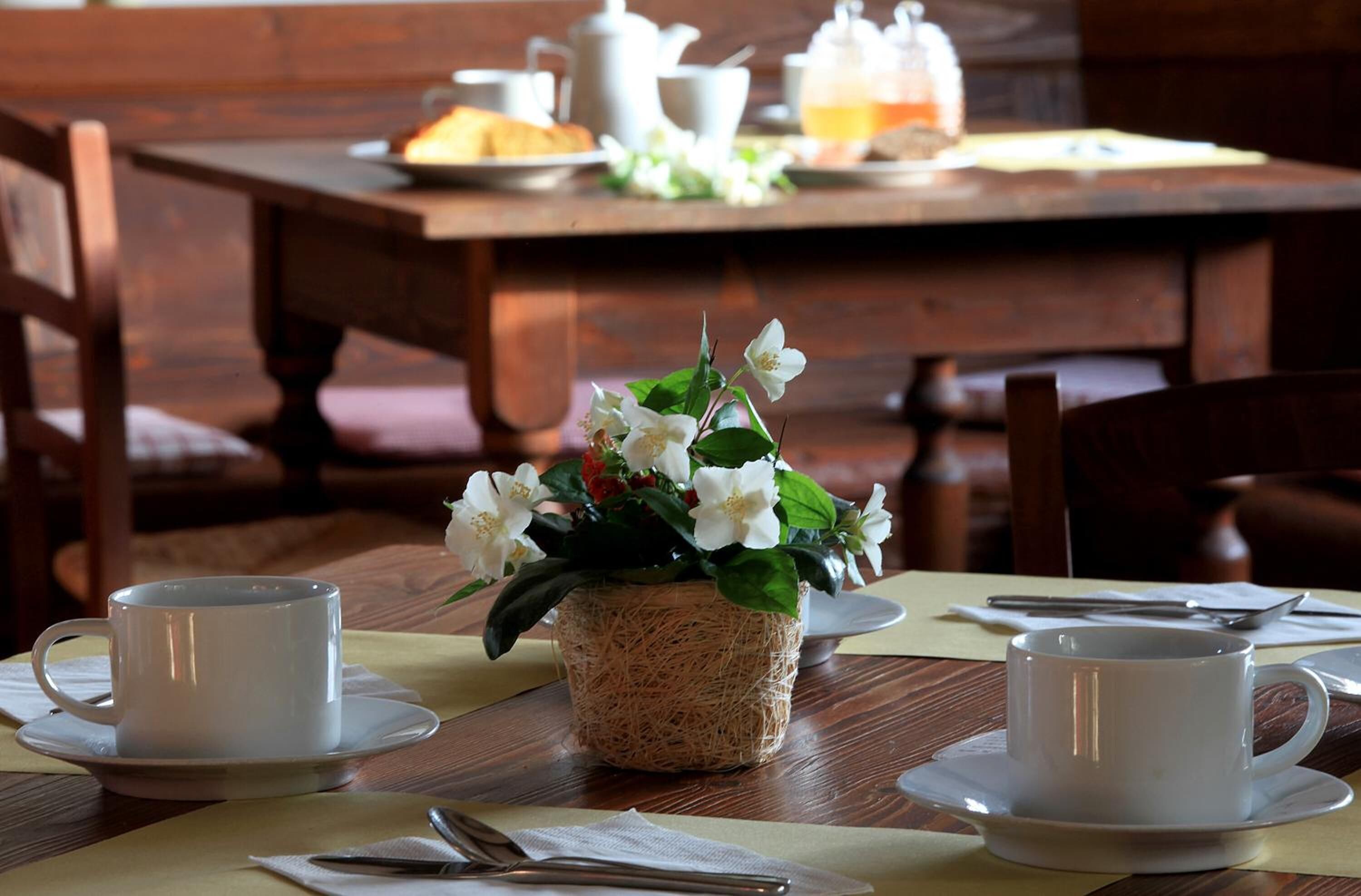 Une table à manger avec des tasses et des soucoupes blanches, ainsi qu’un panier tressé rempli de fleurs.