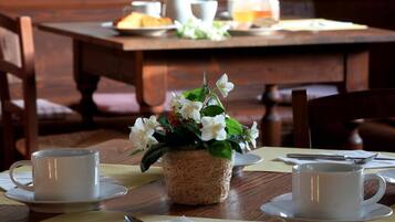 Une table à manger avec des tasses et des soucoupes blanches, ainsi qu’un panier tressé rempli de fleurs.