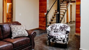 A spacious living area with a leather couch, a patterned pillow, a small table, and a unique animal print chair. A ceiling fan and exposed ductwork are visible. - The Nelson Inn (Sheridan)