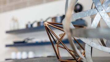 Primer plano de una estructura de alambre de cobre, posiblemente una obra de arte o un mueble, en una habitación con una rueda metálica y estanterías al fondo.