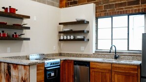 A kitchen with wooden cabinets, a granite countertop, a stainless steel dishwasher, and a brick wall. - The Nelson Inn (Sheridan)