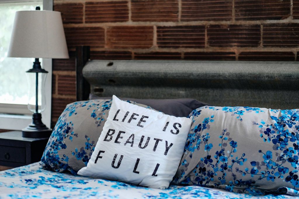 A bed with floral bedding and a pillow with the text "LIFE IS BEAUTY FULL".