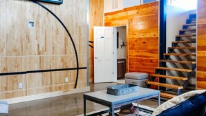 A modern living room with a wooden wall, a staircase, a sofa, a coffee table, and a door leading to another room. - The Nelson Inn (Sheridan)
