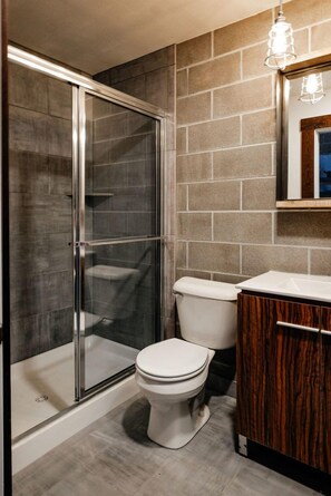 A bathroom with a glass-enclosed shower, a white toilet, and a wooden vanity.
