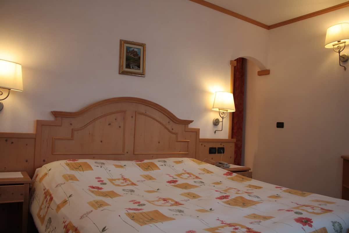 Ein Schlafzimmer mit einem hölzernen Kopfteil, einem floralen Bettüberwurf, zwei Nachttischlampen und einem kleinen Bild an der Wand.