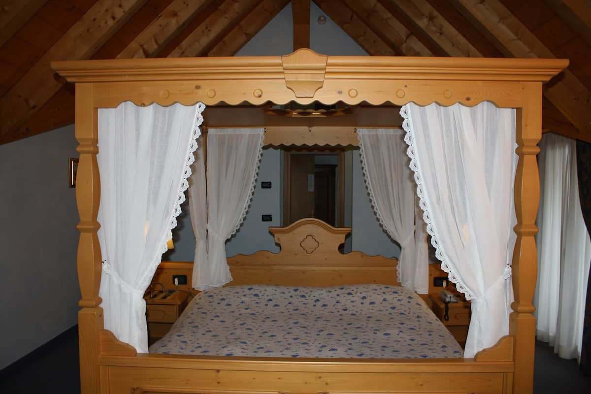 Ein hölzernes Himmelbett mit weißen Vorhängen, einer floralen Tagesdecke und einem Spiegel darüber.
