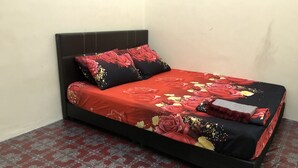 Un lit avec une couvre-lit à motifs floraux rouges et une tête de lit noire, dans une pièce dont le sol est recouvert de carreaux rouges et blancs.