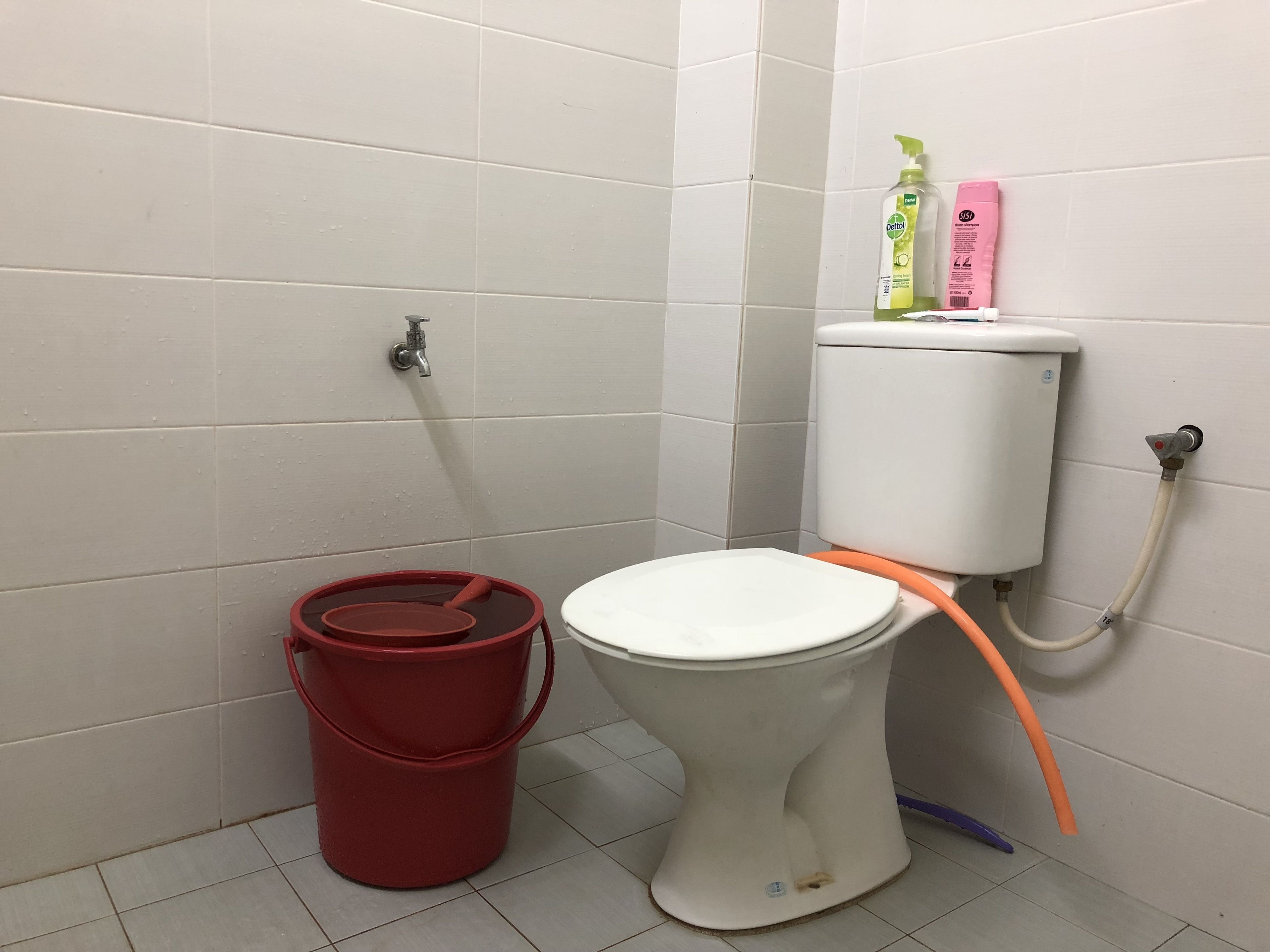 A bathroom with a toilet, a red bucket, and a toilet brush.
