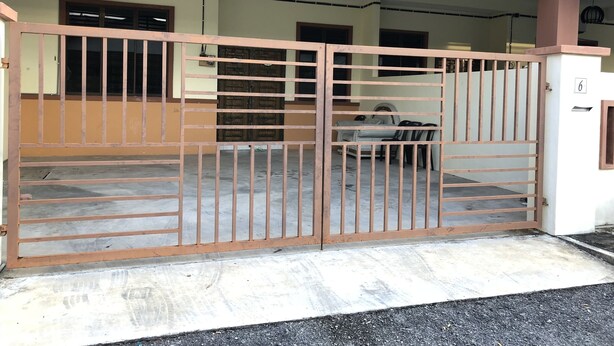 Une entrée fermée par un portail donnant accès à un bâtiment doté d’un sol en béton et d’une grille métallique.