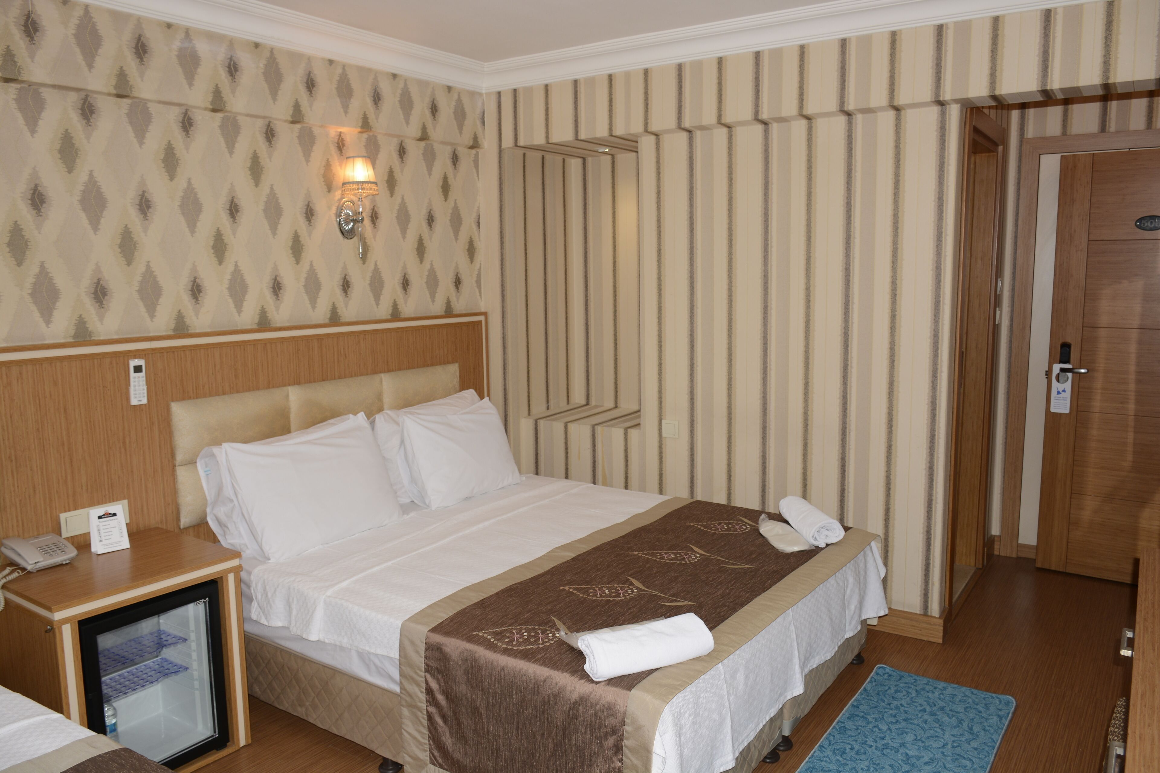A hotel room with a bed, bedside table, and a small refrigerator.