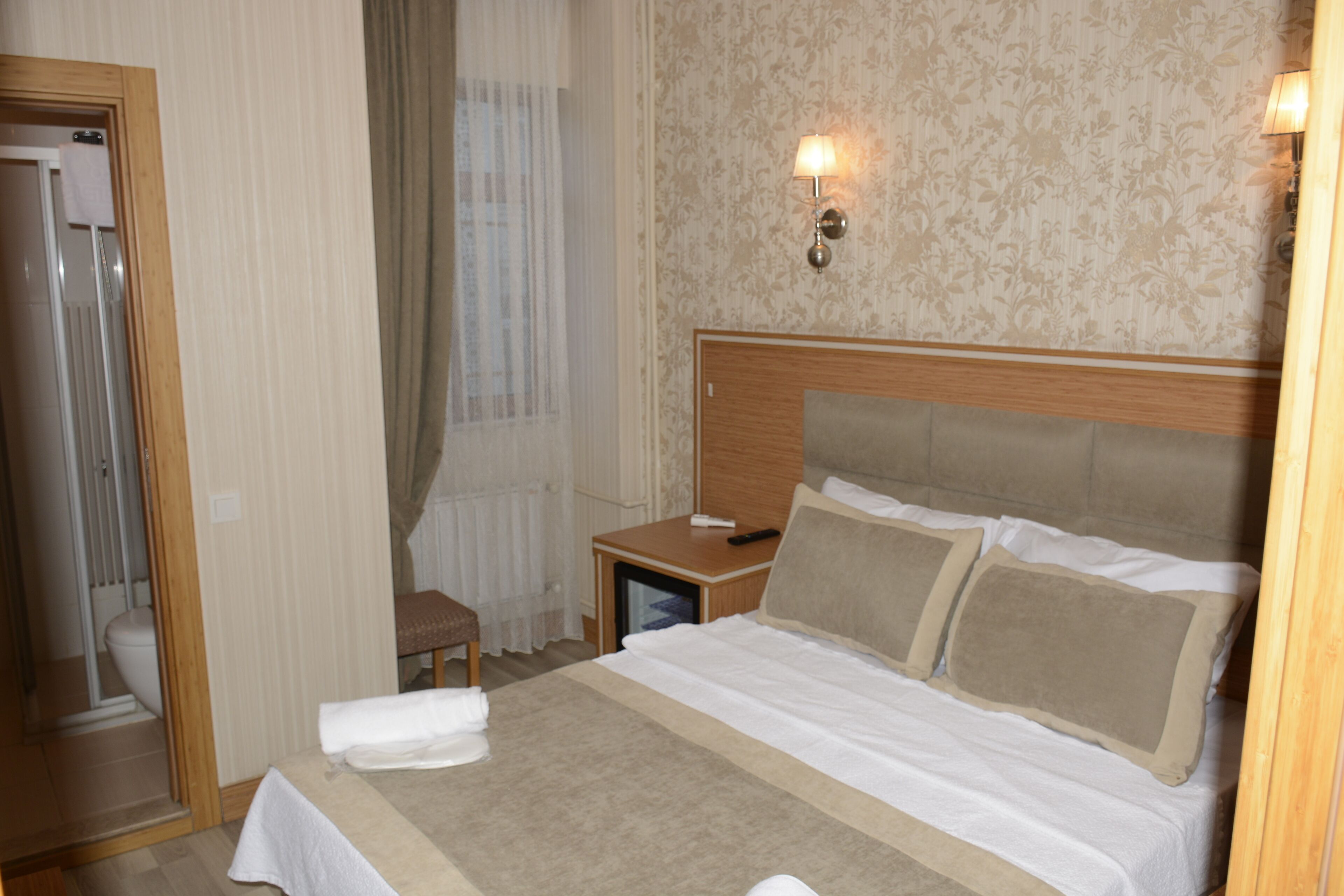 Habitación de hotel con una cama grande, cabecera de madera, mesita de noche, una pequeña mesa y un espejo.