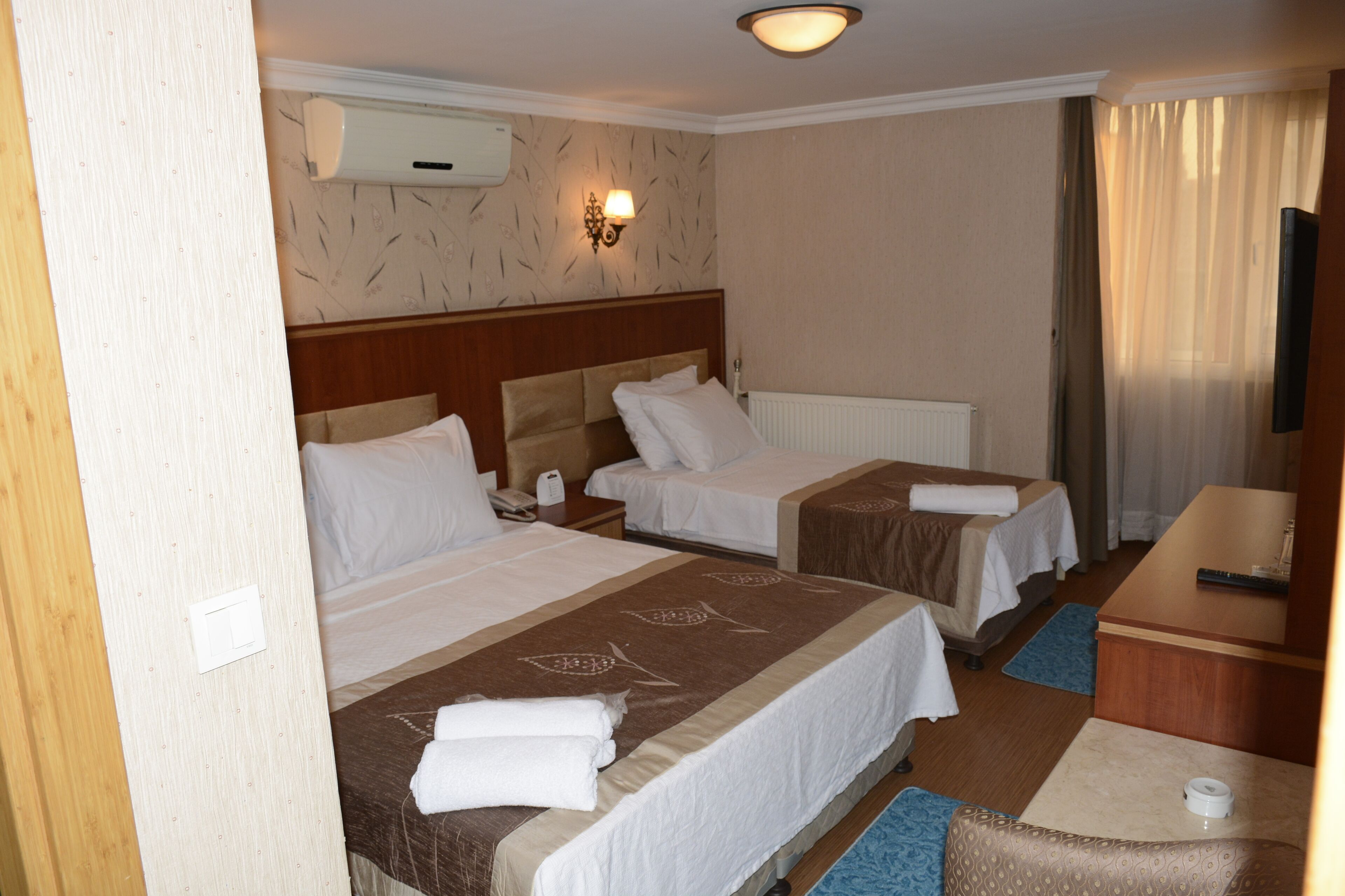 Une chambre d’hôtel avec deux lits, un bureau, une télévision et une fenêtre avec des rideaux.