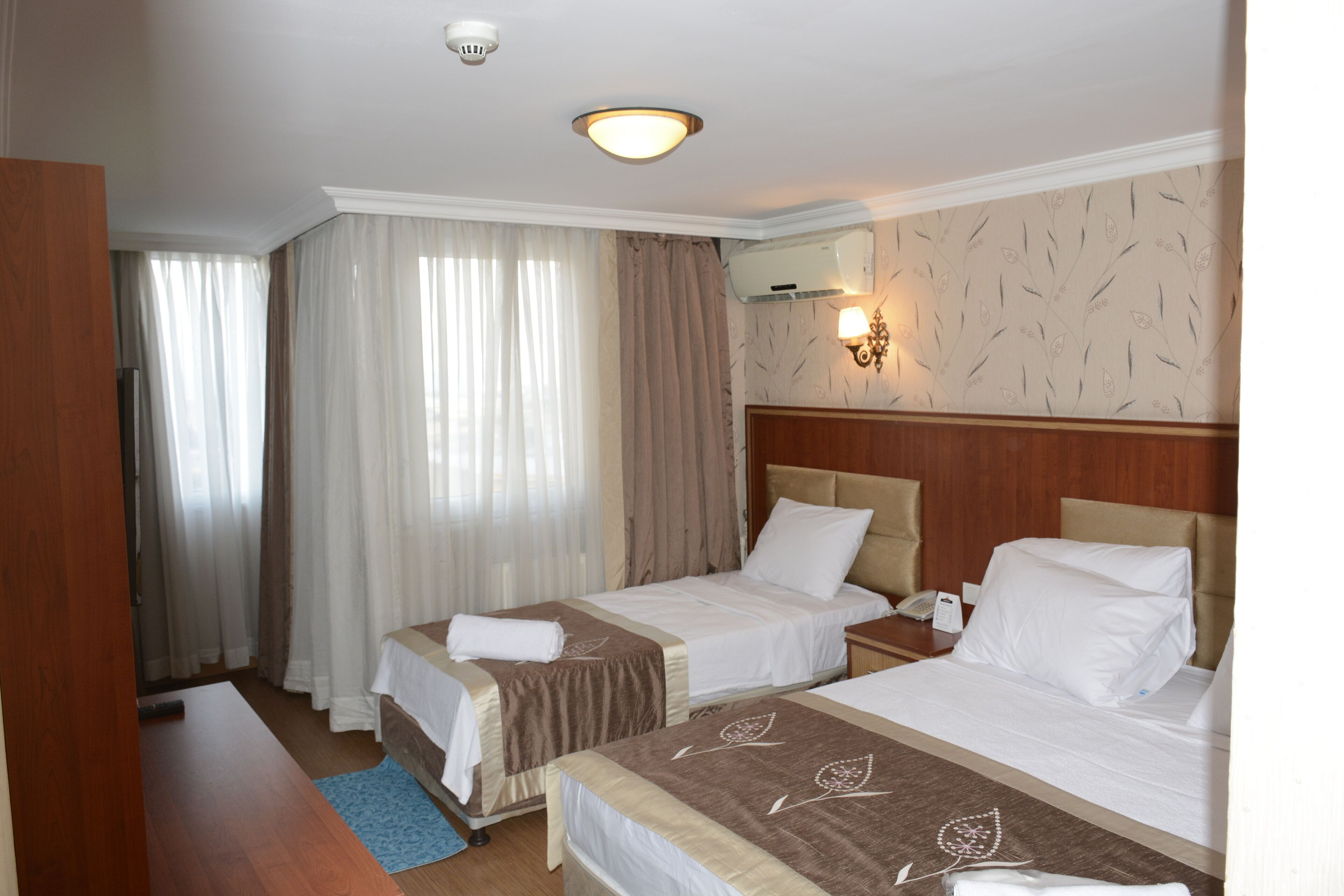 A hotel room with two beds, a wooden headboard, a desk, a mirror, and a window with curtains.
