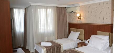 A hotel room with two beds, a wooden headboard, a desk, a mirror, and a window with curtains.