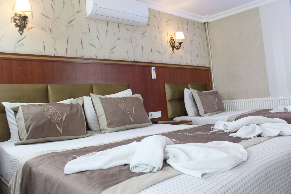 A hotel room with a wooden headboard, two beds with brown and beige bedding, and two wall-mounted lamps.