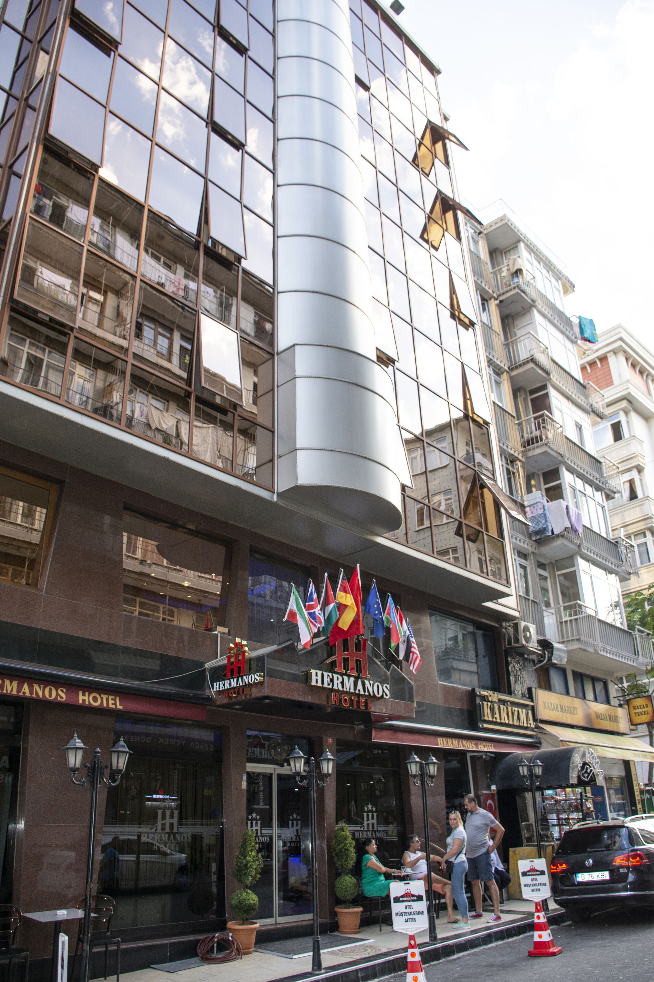 A hotel with multiple flags, a modern glass facade, and a visible entrance with people outside.