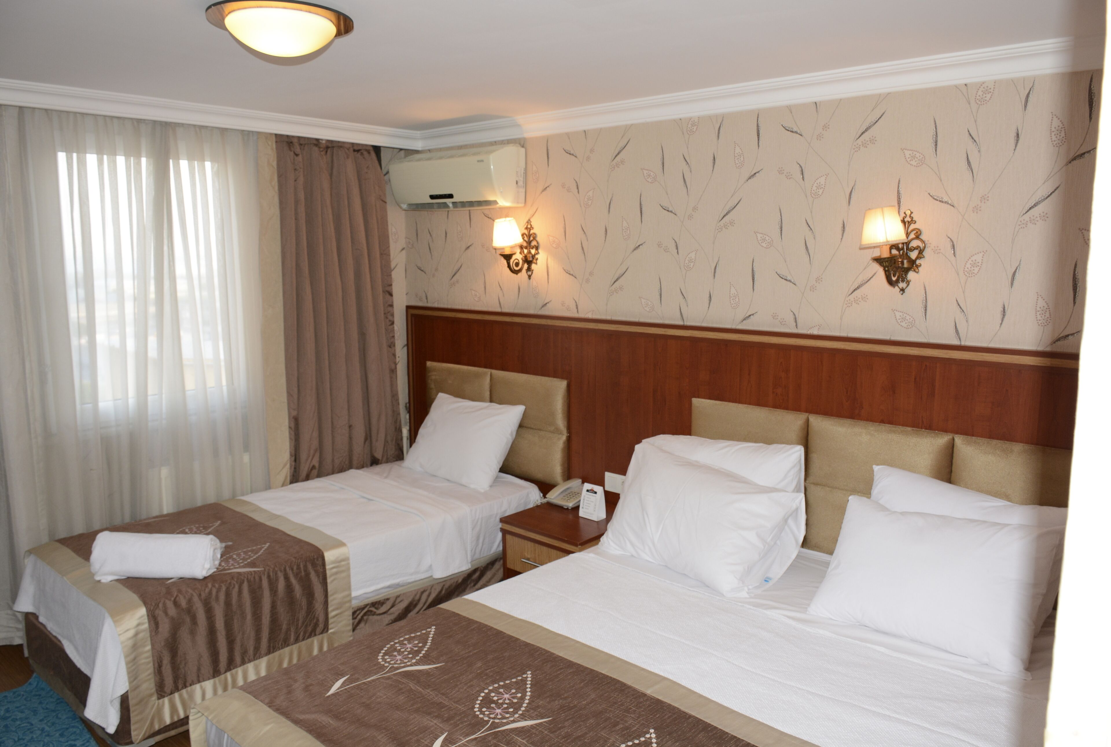A hotel room with two beds, a wooden headboard, a wall-mounted air conditioner, and a nightstand with a lamp.