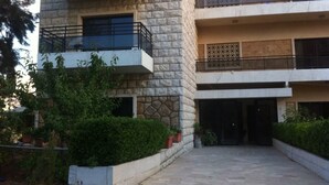 A multi-story building with a stone facade, balconies with metal railings, and a paved entrance area with potted plants. - Wardini (Bhamdoun)