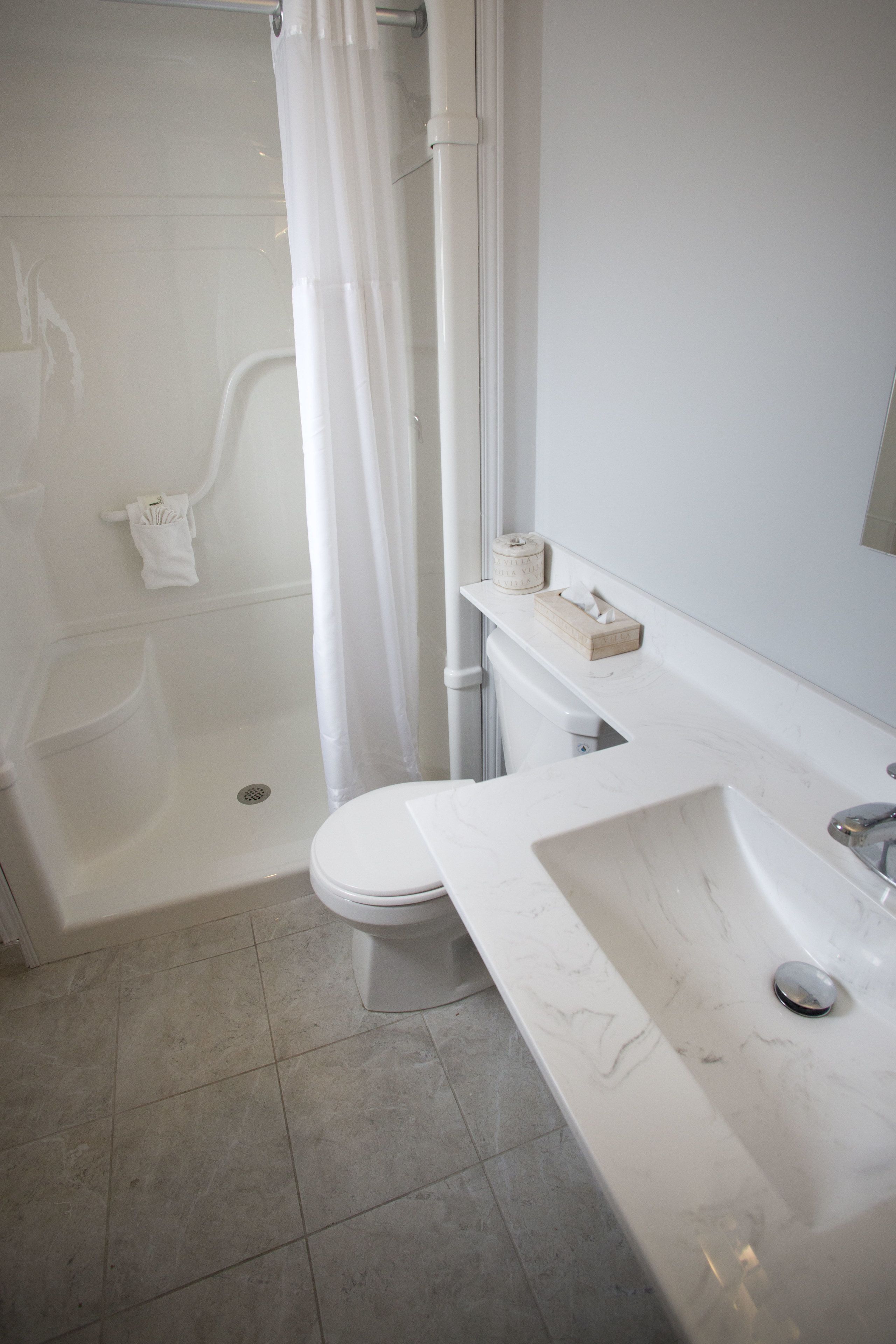 A bathroom with a white toilet, a sink with a marble countertop, a shower with a white curtain, and a towel rack.
