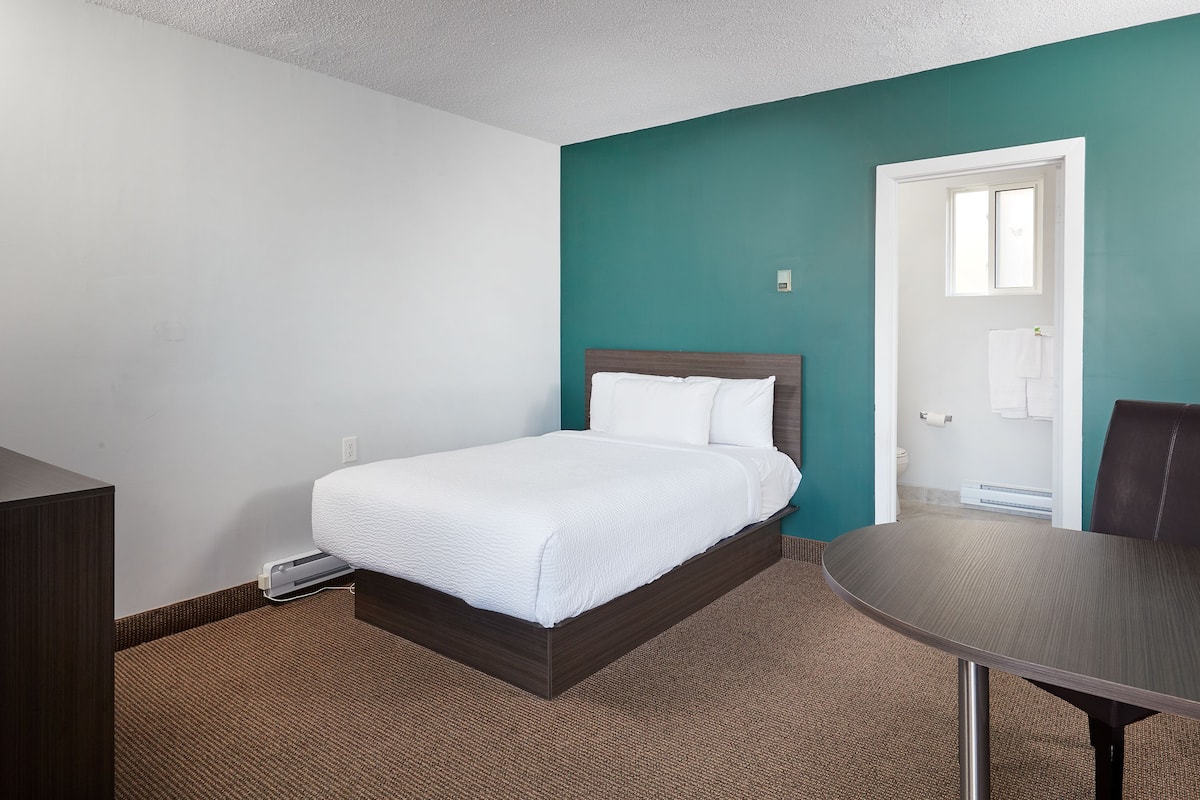 A bedroom with a bed, a table, and a door leading to a bathroom.