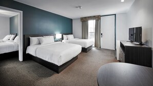 Habitació d'hotel amb dos llits, una taula de treball, un televisor i un finestra gran amb cortines.