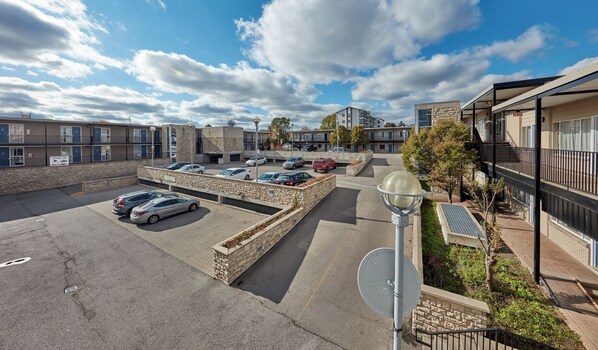 A parking lot with several cars, a stone wall, and a building with multiple windows and balconies.