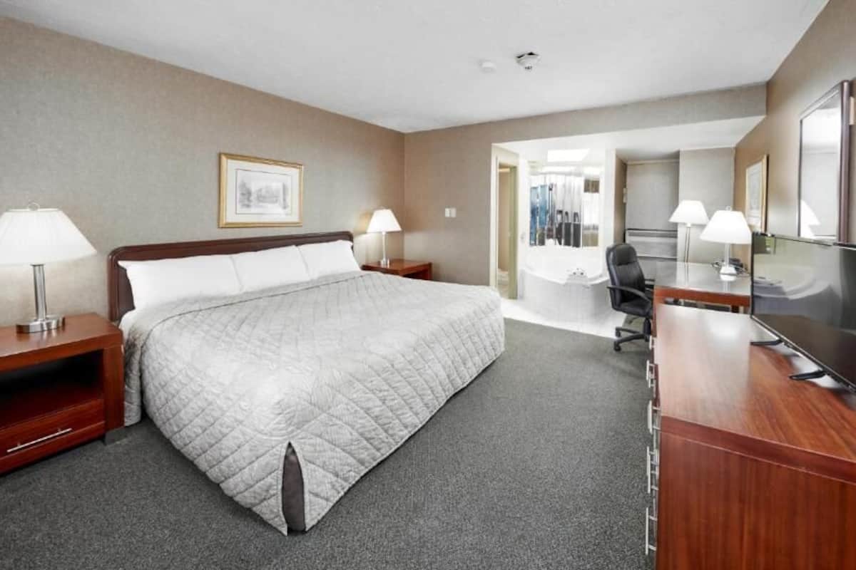 A hotel room with a large bed, bedside tables with lamps, a desk with a flat-screen TV, and a bathroom visible through an open door.