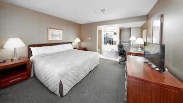 A hotel room with a large bed, bedside tables with lamps, a desk with a flat-screen TV, and a bathroom visible through an open door.