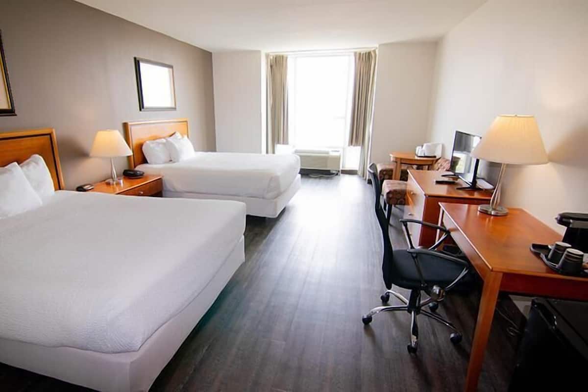 A hotel room with two beds, a desk with a computer, a chair, and a window with curtains.