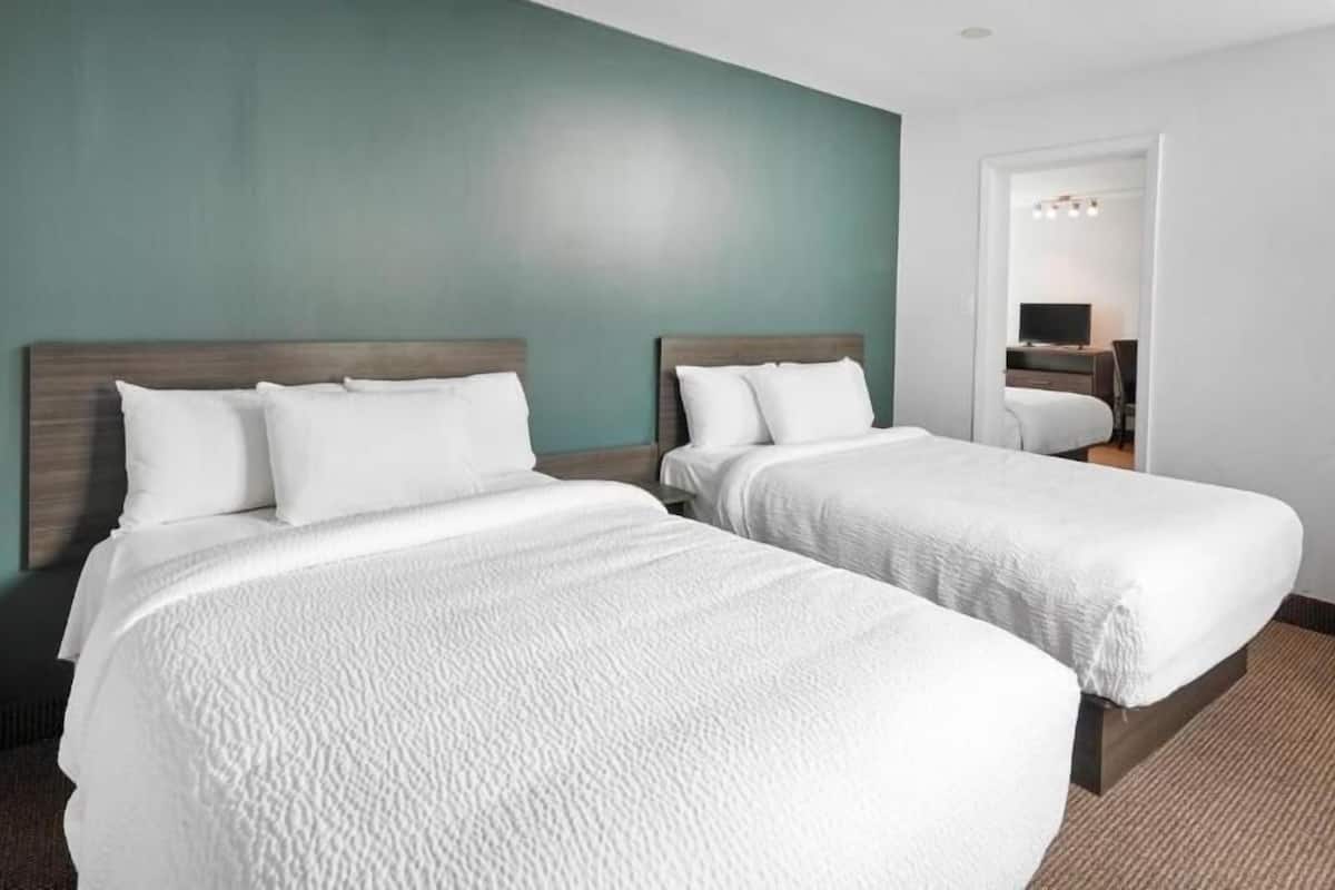 A hotel room with two single beds, a wooden headboard, a teal accent wall, and a carpeted floor.