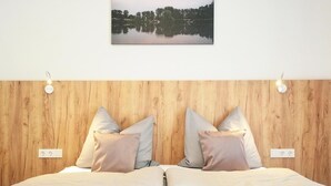 Una cama doble con cabecera de madera, dos lámparas de noche y un cuadro enmarcado con un paisaje de lago.
