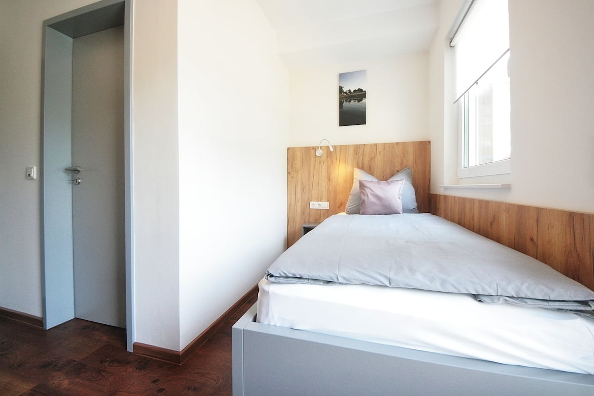 Un dormitorio con cabecera de madera, cama con ropa blanca, mesita de noche y un cuadro en la pared.