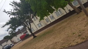 Uma área residencial com casas, uma árvore e um veículo vermelho estacionado na rua.