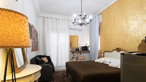Habitación de hotel con cama, escritorio, silla, cómoda, espejo, candelabro y ventana con cortinas.