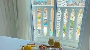 Un safata d'esmorzars amb ous, fruita i suc a un balcó amb vista a la ciutat.