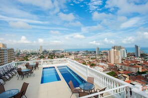 Área de piscina en la azotea con vista a la ciudad, que incluye edificios altos y una costa.