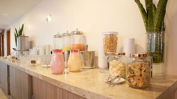 Een ontbijtbuffet met diverse bakken en flesjes met eten en drinken, waaronder cornflakes en vruchtensappen.