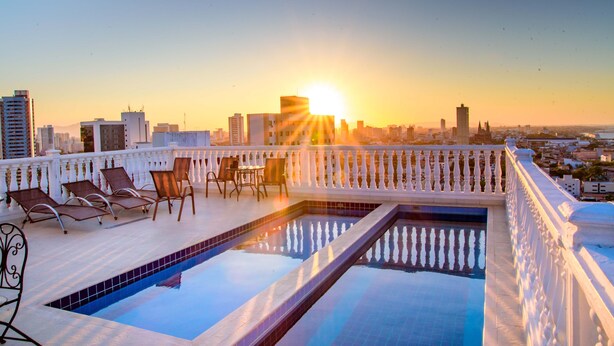 Una piscina a la terrassa amb gandules i una vista panoràmica de la ciutat al capvespre.