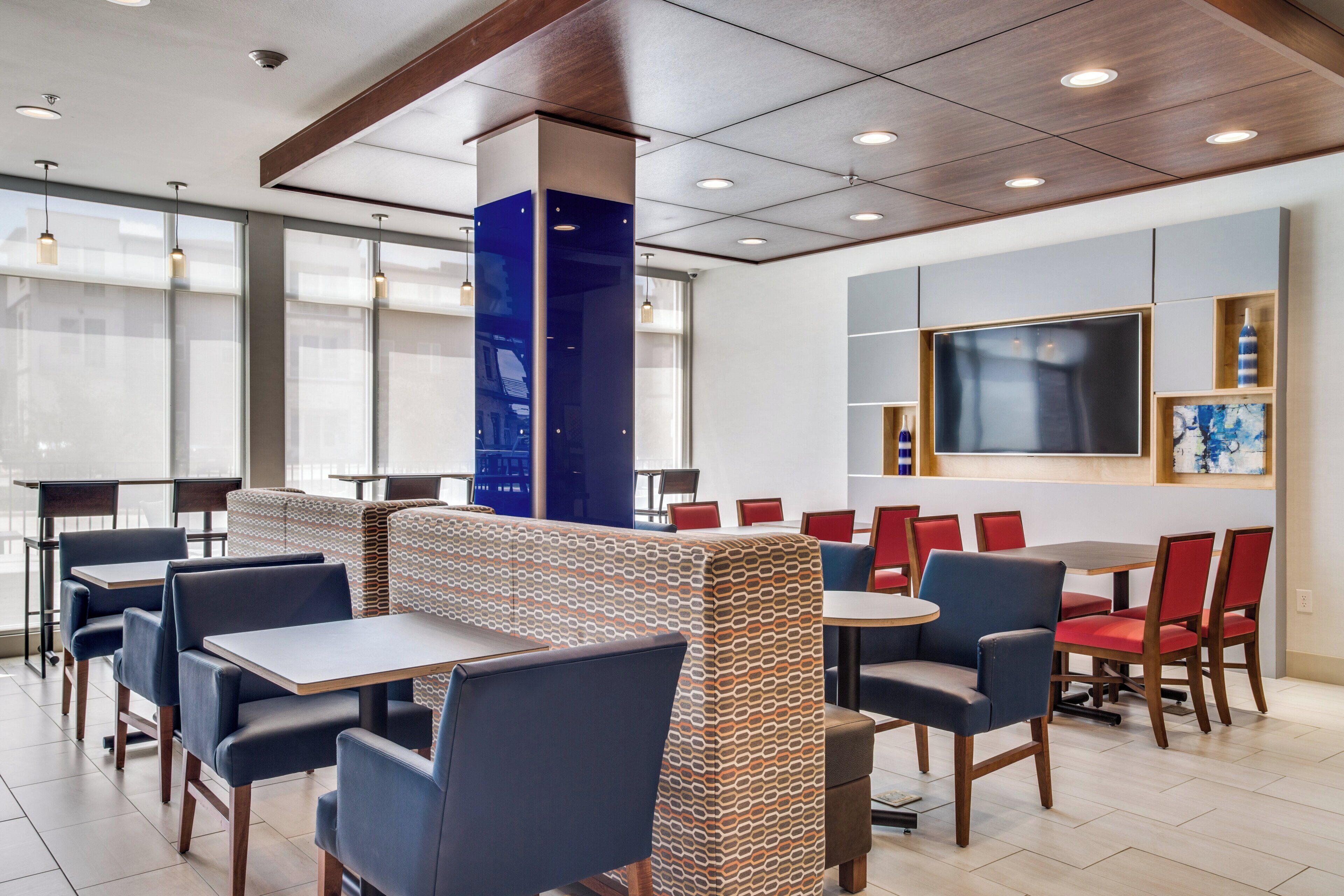Un intérieur de restaurant moderne avec des tables hautes et des banquettes, de grandes fenêtres et un pilier central.