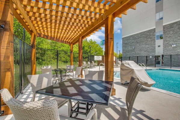 An outdoor pool area with a covered seating area, poolside chairs, and a table. - Holiday Inn Express & Suites Denton South by IHG (Denton)