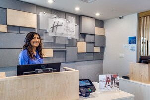 A hotel reception desk with a modern design, a digital check-in kiosk, and a sign indicating check-in times.