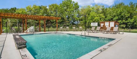 A clear swimming pool with lounge chairs and a wooden pergola.