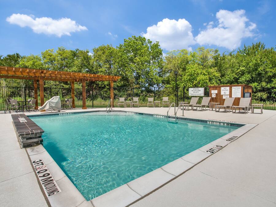 A clear swimming pool with lounge chairs and a wooden pergola.