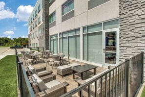 An outdoor seating area with wicker furniture and a view of a building with large windows. - Holiday Inn Express & Suites Denton South by IHG (Denton)