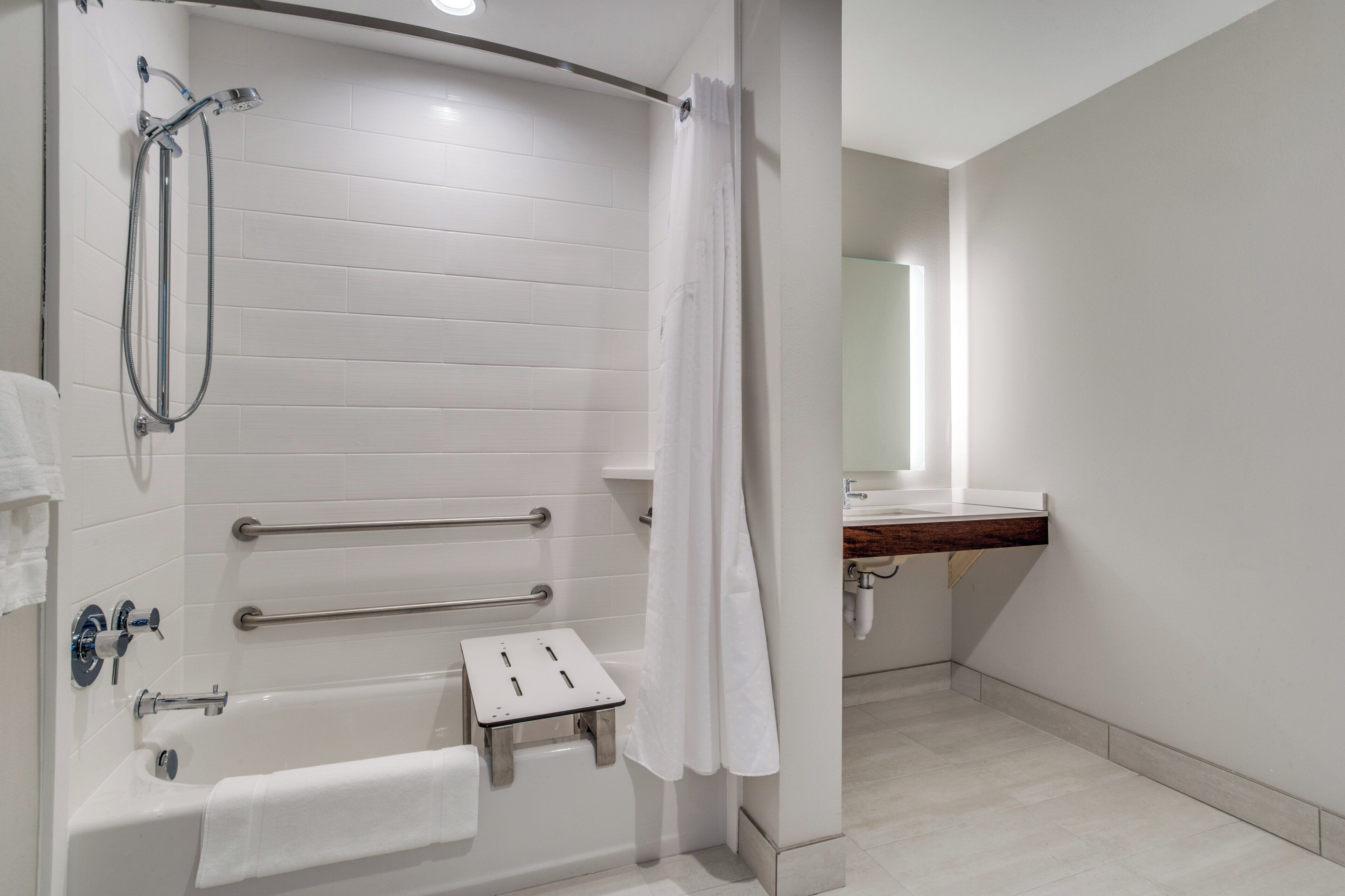 A modern bathroom with a white tiled shower, a bathtub, a small step stool, and a vanity with a mirror.