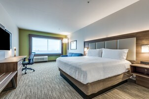 A hotel room with a large bed, a desk, a chair, a television, and a window.