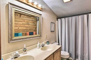 Kylpyhuone, jossa on puinen allaskaappi, kaksi pesuallasta, peili ja suihkuverho.