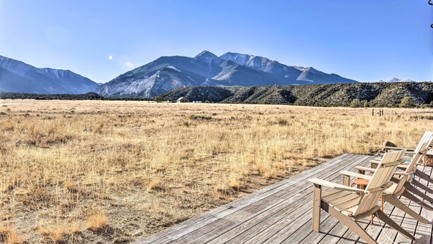 Eine Holzterrasse mit Stühlen mit Blick auf ein trockenes Grasfeld und Berge im Hintergrund.