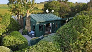 Un cottage con tetto verde, un camino in pietra, un patio con una panchina e antenne satellitari.